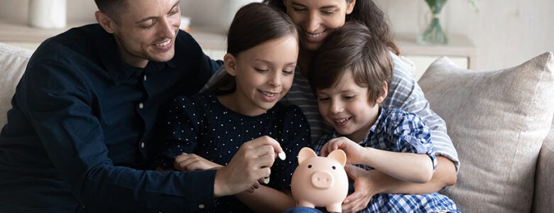 Happy family teaching kids about saving money with a piggy bank while sitting together on a couch at home