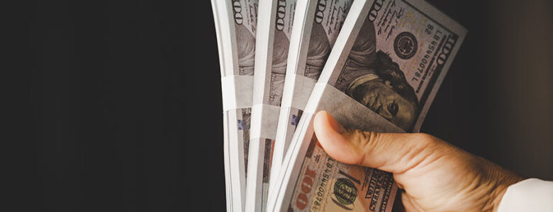 A hand holding stacks of $100 bills, representing cash flow and funding from hard money real estate loans