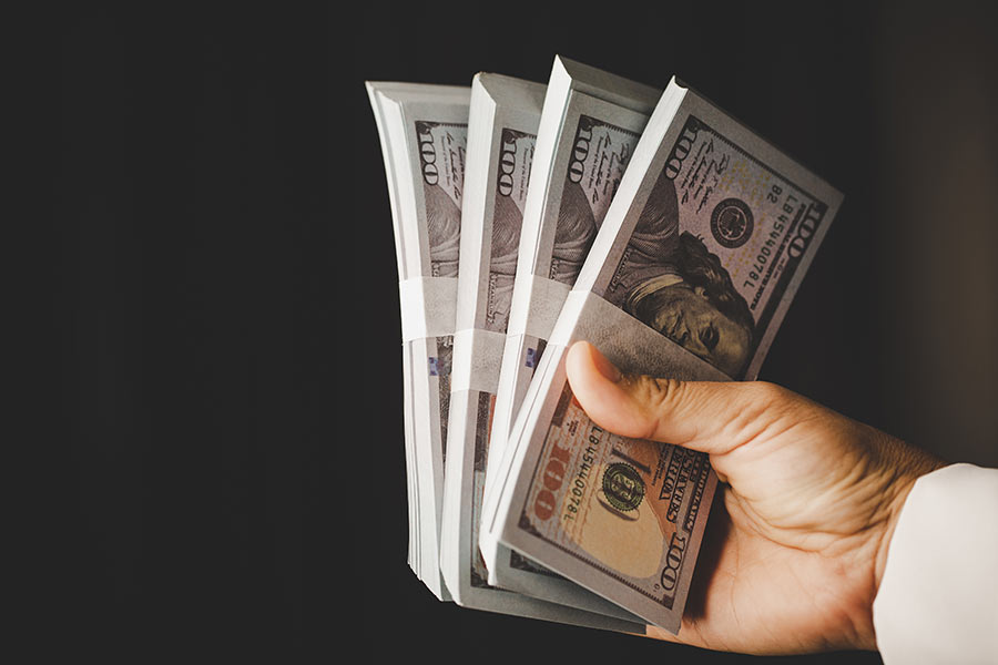 A hand holding stacks of $100 bills, representing cash flow and funding from hard money real estate loans